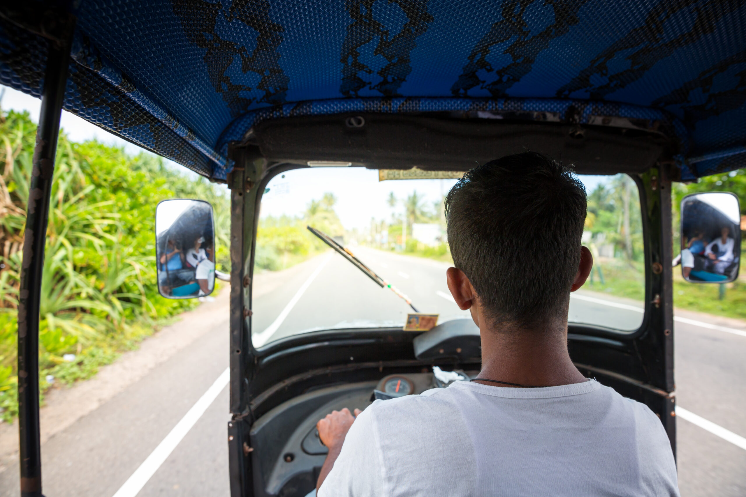 Tuk tuk driver on road of Sri Lanka, view from car. Ceylon traditional tourist transport, local taxi